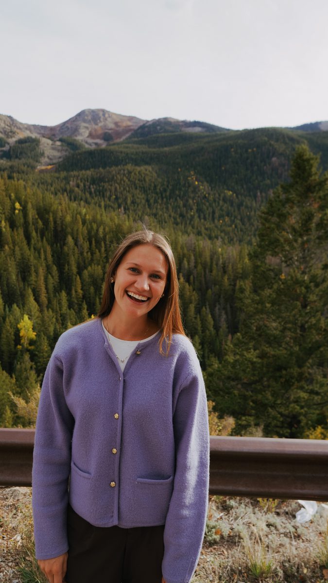 Kayla Greenwood smiling outdoors in the mountains, wearing a lavender cardigan