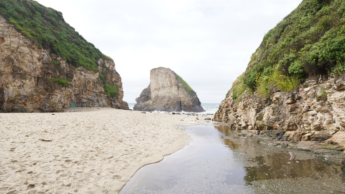 A sandy cove with a sea stack rock formation and cliffs